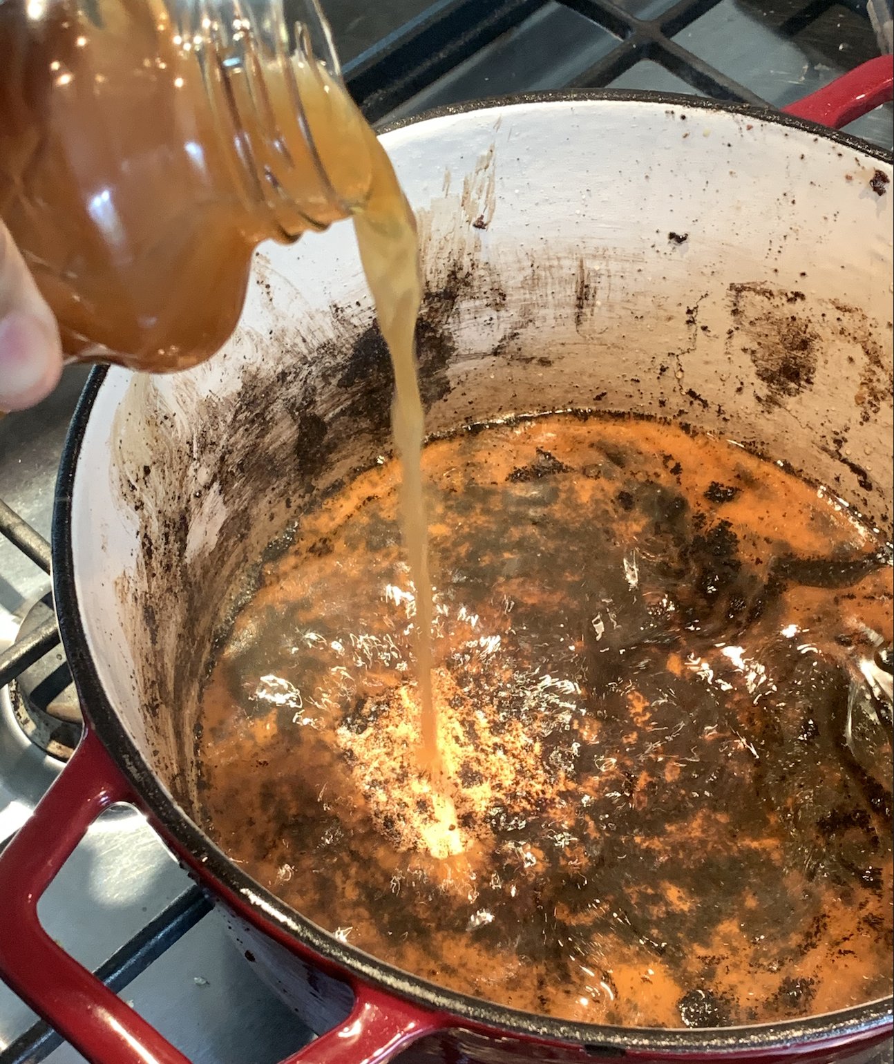 Dutch oven with pork burnt spices and pork shoulder bits being deglazed with apple cider