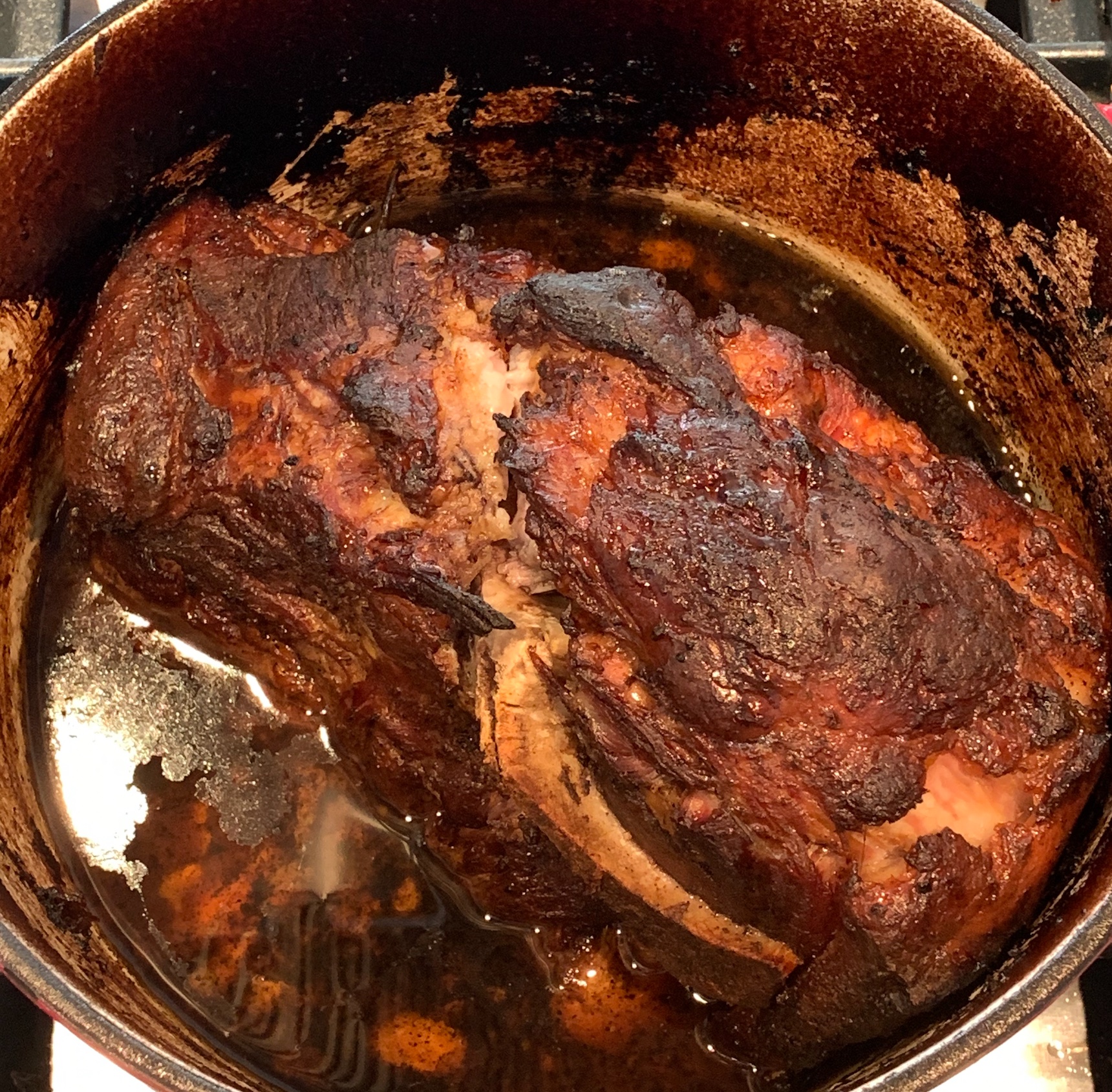 A cooked, magohony color pork shoulder in the dutch oven